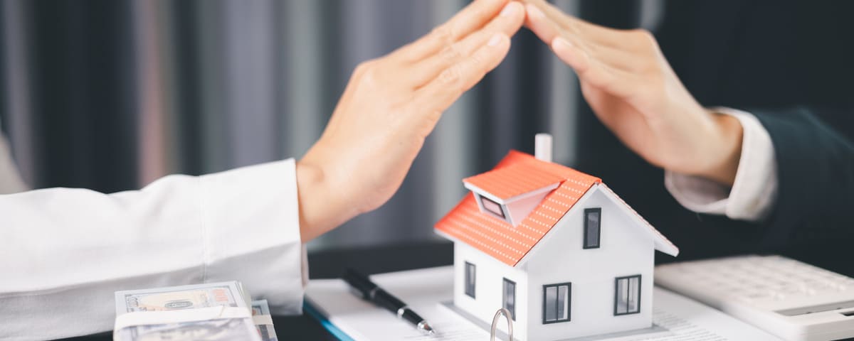 Agent immobilier ou assureur protégeant une maquette de maison avec ses mains, symbolisant l'assurance, lors de la signature d'un contrat avec un client